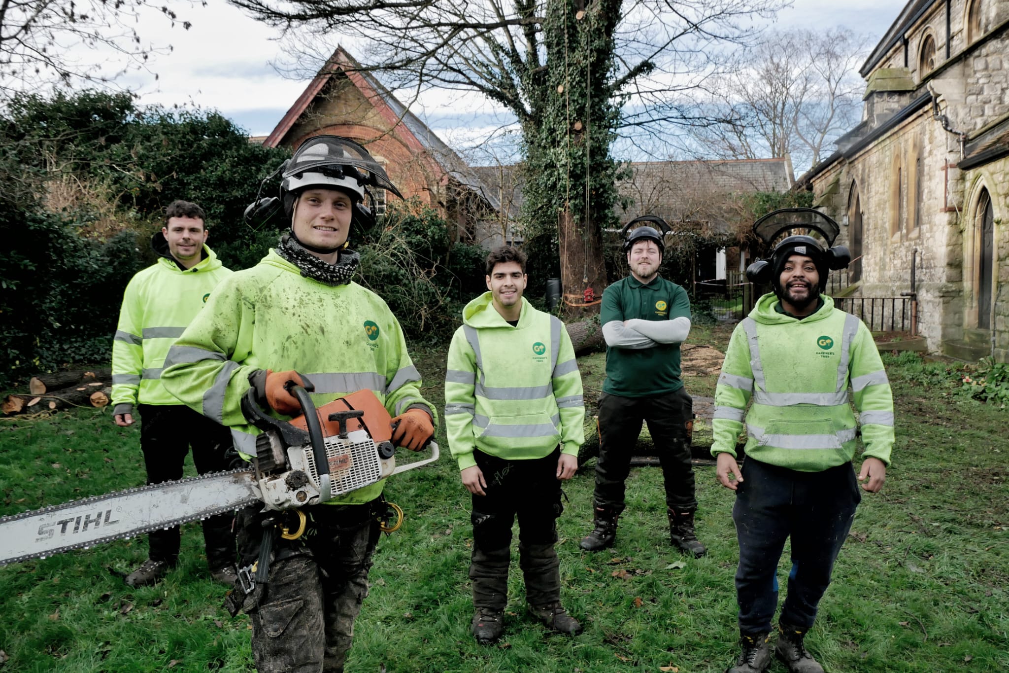 Gardner’s Trees team standing on site with chainsaw and climbing helmets. Gardner’s Trees team standing on site with chainsaw and climbing helmets.